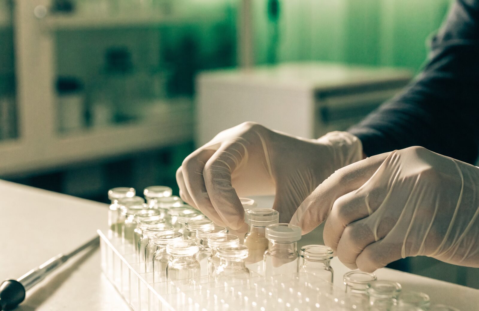 Gloved hands arranging clear glass vials in a rack on a research laboratory bench