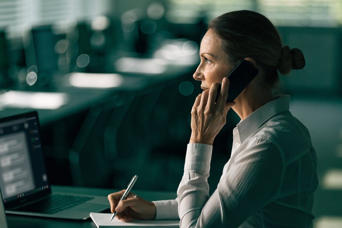 An operations manager turned away from her laptop, verifying an answer by phone and taking notes