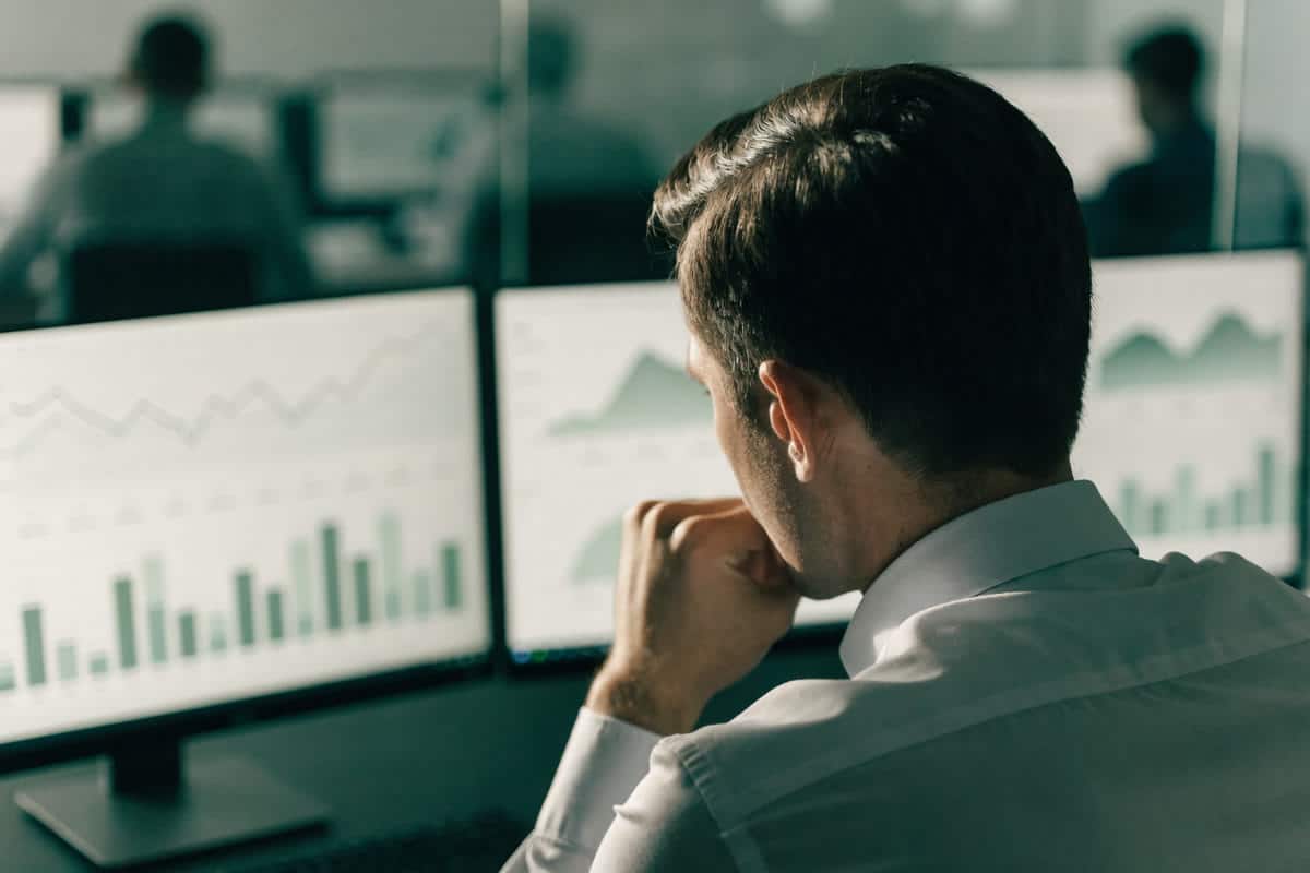 A risk analyst at a bank reviewing account activity charts on two monitors in a quiet office