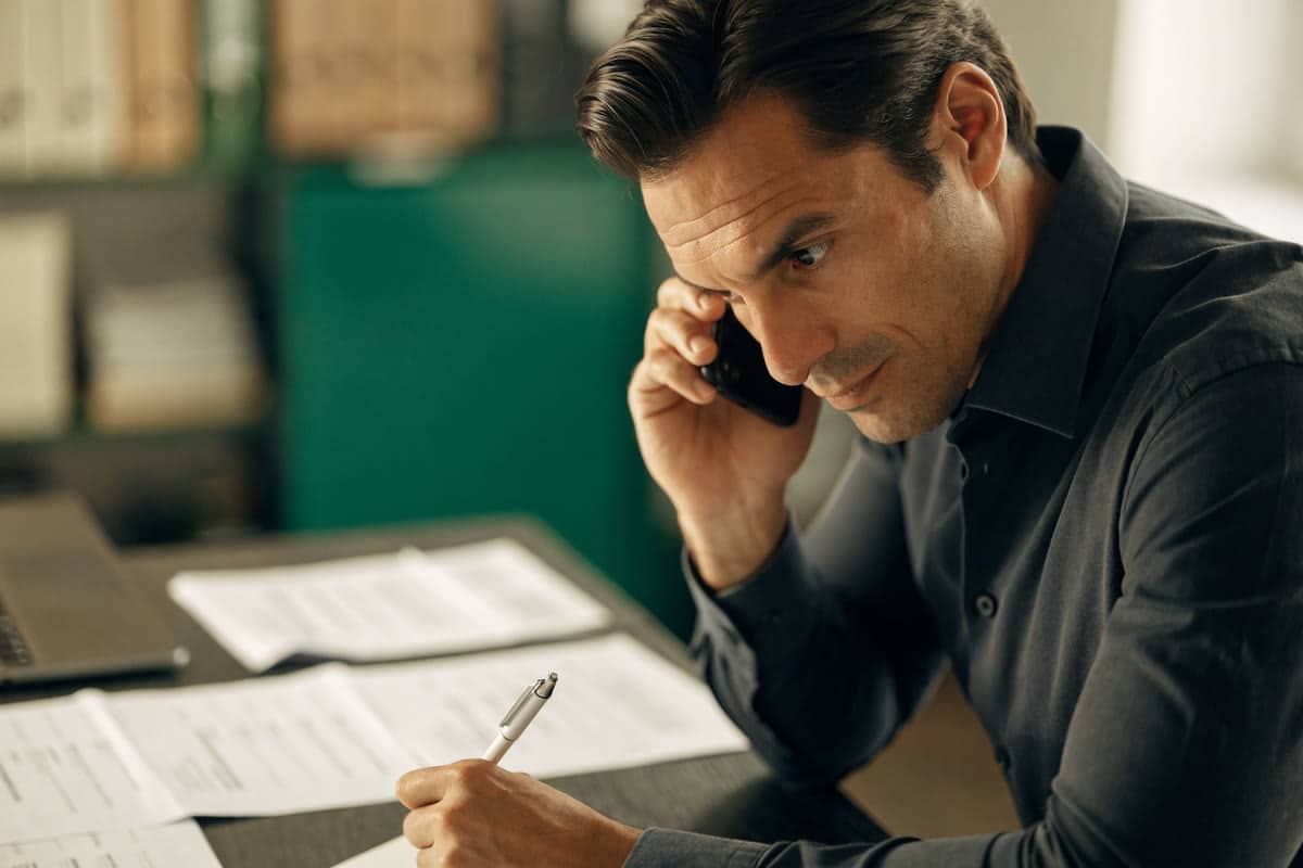 A business owner on the phone at a desk with printed bank statements and a pen, taking notes